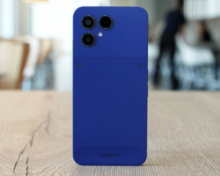 The back of the cobalt blue Fairphone 6+ stood up on a wooden table.