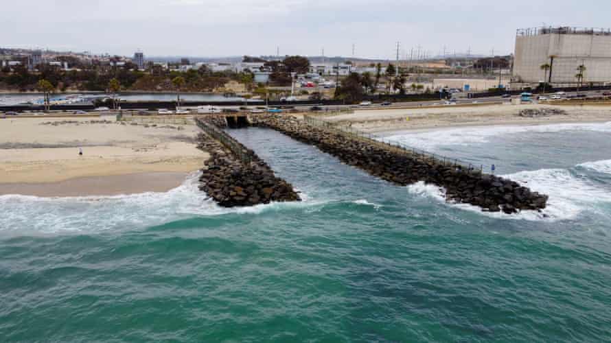 A man fishes on a rocky jetty off a beach.