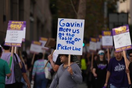 a man holds a sign that reads ‘Gavin meet us at the table or the picket line’