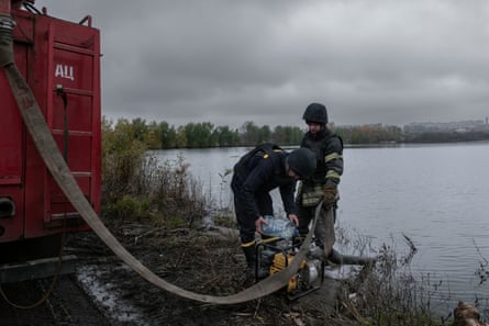 Firefighters use a hose from a lake to refill water reserves in their red fire engine