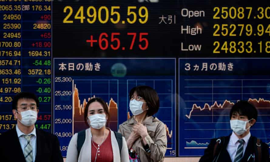People stand in front of an electronic board displaying the Nikkei 225 index in Tokyo on 10 November 2020.