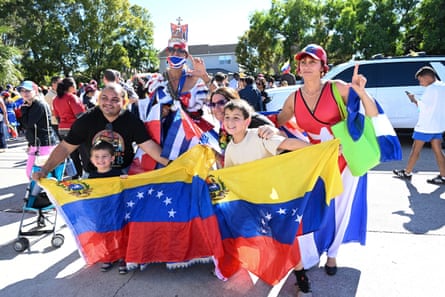 Kids and adults gather around a Venezuelan flag and flash the peace symbol for a photo.