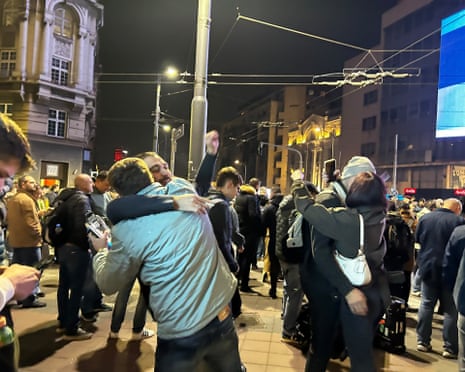Belgrade crowds celebrate at night, with two people embracing after Vučić's election concession