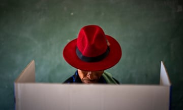 A person in a red hat stands in a voting booth
