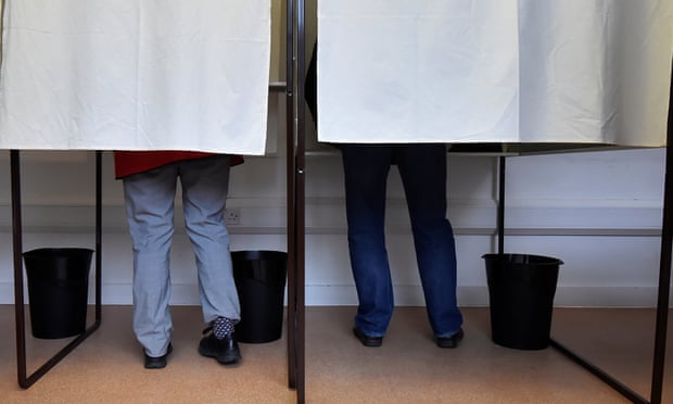 Voting booths, with voters' legs showing under drawn curtains