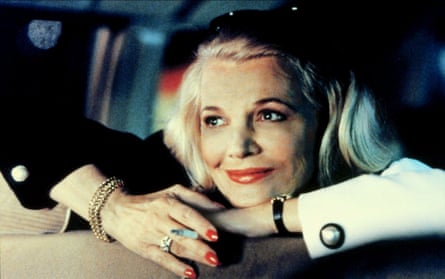 Sitting in the back of a cab, she rests her head and arms on the seat in front and smiles