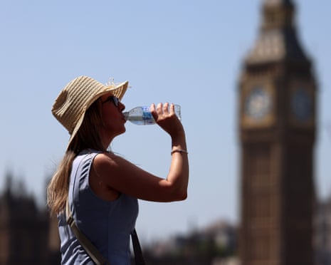 A woman wearing a hat drinks water, with the parliament building in the background