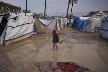 A Palestinian boy walks through an area in a temporary tent camp after heavy rainfall