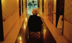A woman in a wheelchair looking down a long dark corridor of an aged care home
