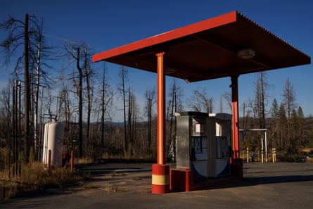 A red canopy over two gas pumps on a stretch of asphalt with burned trees beyond it.