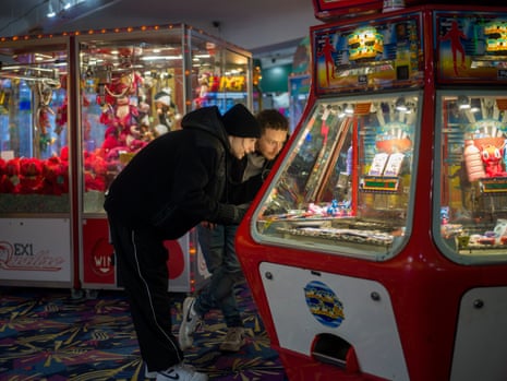 A young woman and a young man peer at a games machine in an amusement arcade