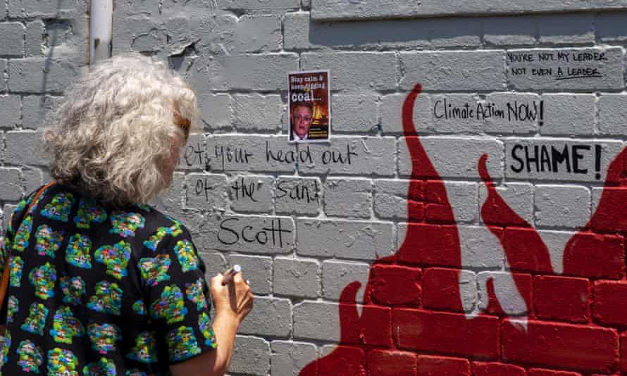 A woman writes a comment on the wall next to a mural of Scott Morrison