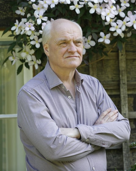 James Anderson stands with his arms folded in a garden.