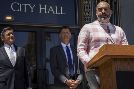 A man stands at a podium in front of a building labeled 'City hall'.