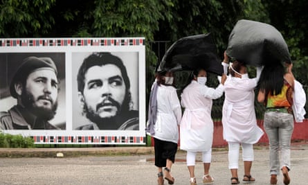 Cuban doctors, protecting themselves from the rain with plastic bags, pass by images of Fidel Castro and Che Guevara before departing to Kuwait to assist with the coronavirus outbreak, in Havana on Thursday.