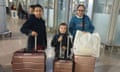 Two young boys and girl with sad expressions on their faces stand with their luggage in an airport