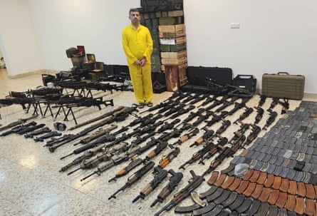 Al-Jumaili in a yellow jumpsuit, surrounded by weapons and boxes of ammunition.