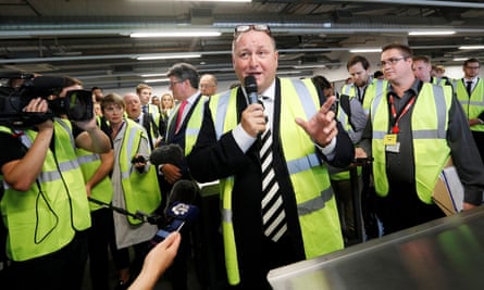 He holds microphone surrounded by people in hi-vis jackets