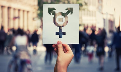 Hand holding a paper sheet with transgender symbol and equal sign inside. Equality between genders concept over a crowded city street background. Sex