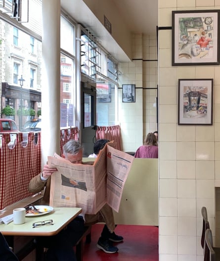 Man reading a newspaper at the window of Regency Cafe, Pimlico, London.