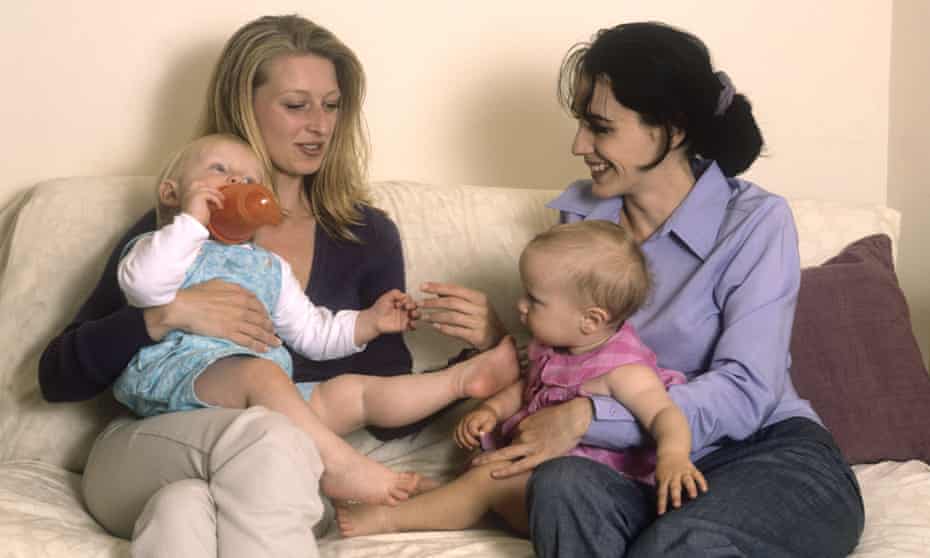 Stock image: Two mothers sitting on a sofa chatting with their toddlers
