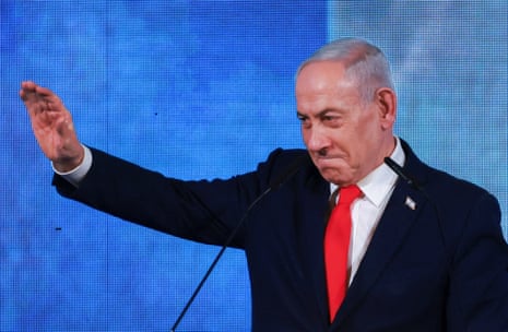 Benjamin Netanyahu raises one arm while speaking at microphones, with a blue backdrop