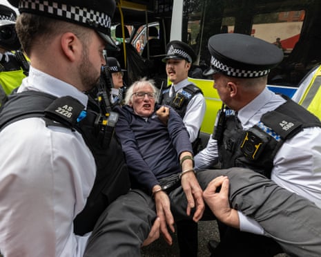 Police officers carry an older, handcuffed man into a police van