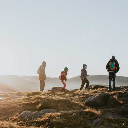A father enjoys a view with his three young children. They have a sense of achievement after scaling a mountain. The sun is low.