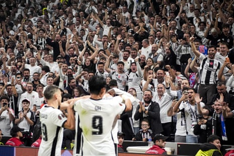 Besiktas fans cheer with raised arms as players embrace after scoring a goal
