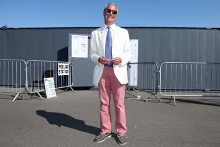 Farage wearing a white blazer and pink trousers standing outside a grey building