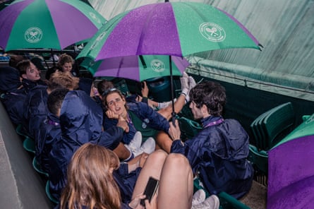 Ball girls and ball boys wait under umbrellas for the rain to stop