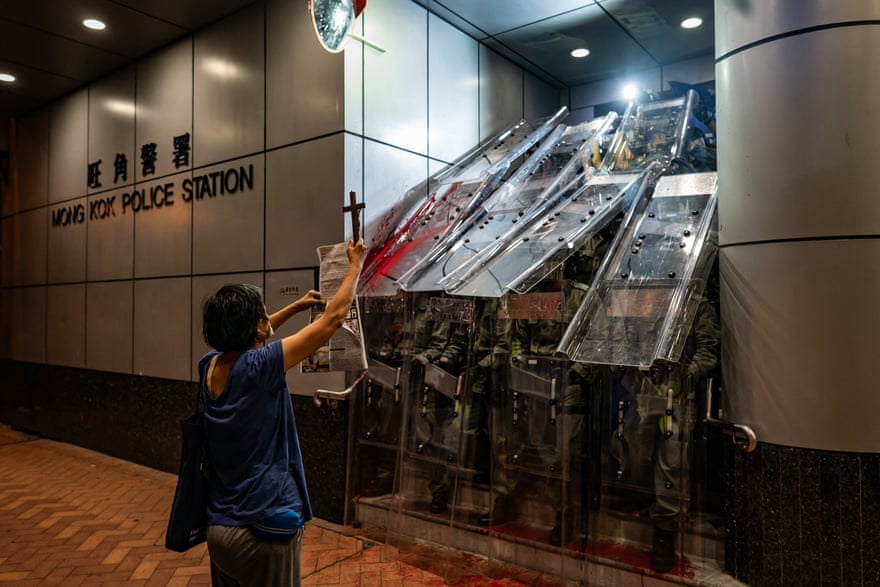 A woman holds a cross in front of the Mongkok Police Station as riot police holding shields stand guard during a standoff with protesters after an anti-government rally in September.