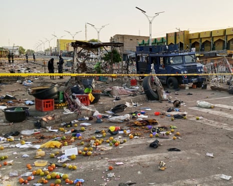 Police tape across the road and fruit and debris scattered over the ground, with a police van and officers in the background