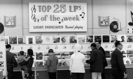 A group of people stand in the aisle of a record store, looking through record racks. The Mamas And Papas are number one.