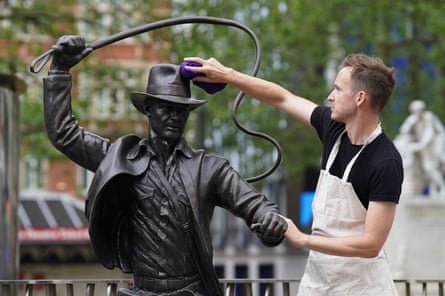 A life-sized bronze statue of the character Indiana Jones being cleaned as it's unveiled in Leicester Square in 2023.