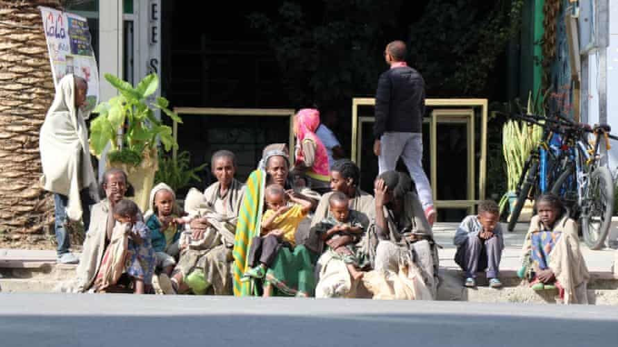 Women and children sit on street kerb.