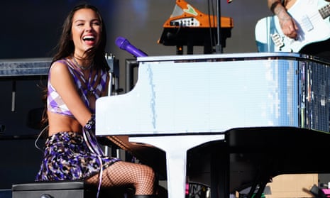 Rodrigo smiles as she sits playing piano onstage