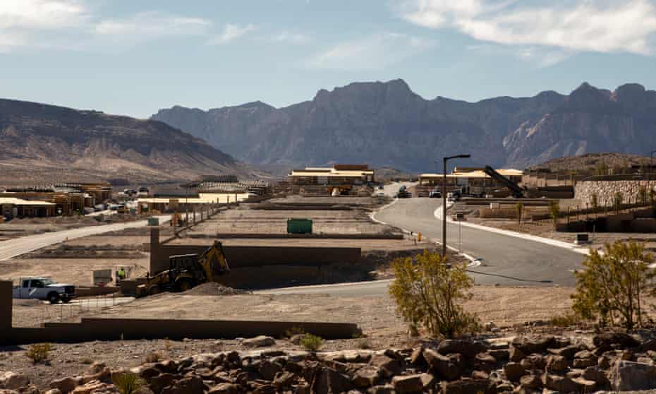 A bulldozer is seen in the foreground of a housing development being built in a very dry area of Las Vegas, with large mountains in the background.