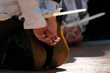 A person's hands are bound behind their back with white plastic zip ties.