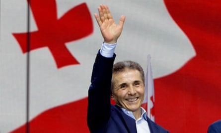 Bidzina Ivanishvili waves during a rally as he stands in front of red and white Georgian flag