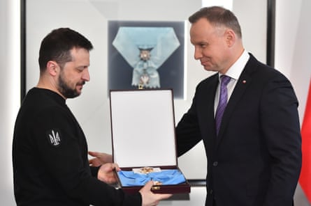 Volodymyr Zelenskyy holds an open presentation box with a medal inside it as Andrzej Duda reaches out to congratulate him