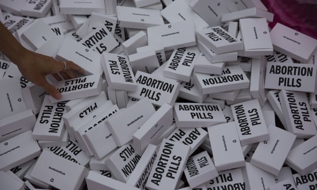 A hand reaches into a pile of white medicine boxes with Abortion Pills written on it