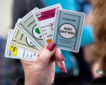 A woman holds four Monopoly Deal cards.