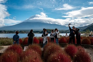 Tourists across the water from Mount Fuji take selfies and look at their smartphones