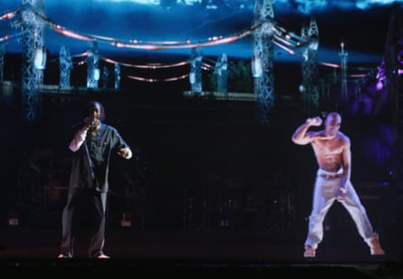 Snoop Dogg in black performs on stage next to a topless hologram of Tupac.