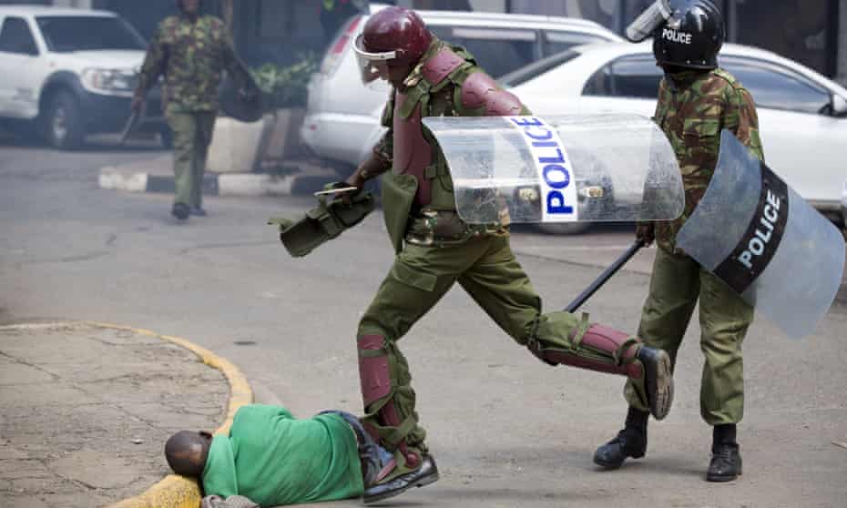 A Kenyan riot policeman repeatedly kicks Boniface Mosoti as he lies in the street.