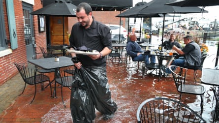 Waiter wading through shallow water on patio and customers sitting at table in water