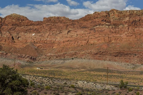 A vast landscape leading up to a mesa shows a home surrounded by dry land.