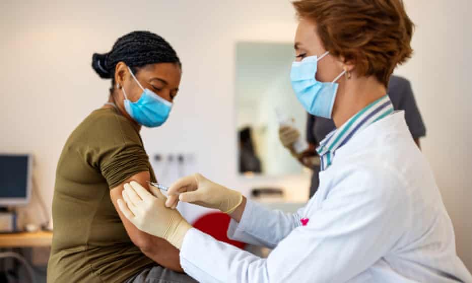 General practitioner giving flu shot to a senior woman<br>Posed by models Female doctor wearing a face mask giving vaccine to a patient in her clinic