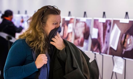 A woman covers her mouth in horror as she looks at a gruesome collection of images of dead bodies in Syria